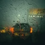 Image of car driving through the rain with view of car in front through wet windscreen