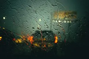 Image of car driving through the rain with view of car in front through wet windscreen