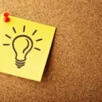 Image of post-it note on corkboard with light bulb shining drawn on the post-it note to illustrate post