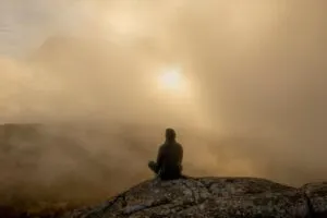 Image of a person sat at the top of a hill where the sun is barely visible through the clouds to illustrate post