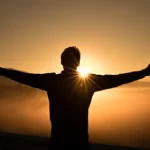 Image of person throwing arms out in celebration of the sun