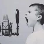 Image of boy forcefully using his voice through a spitguard on to a microphone to illustrate post