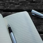 Image of cartridge pen on notebook with lid lying aside on the slatted table used to illustrate post