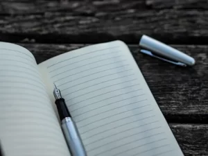 Image of cartridge pen on notebook with lid lying aside on the slatted table used to illustrate post